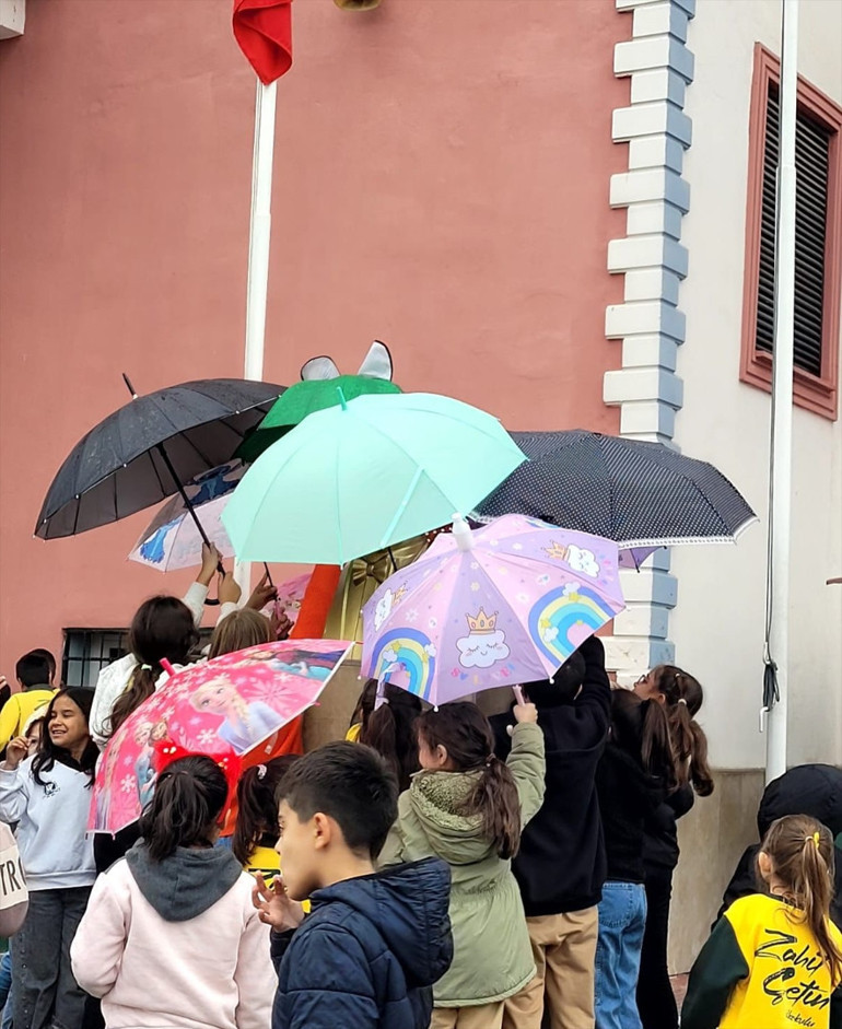 Bir grup öğrenci büstü şemsiyeyle yağmurdan koruyor